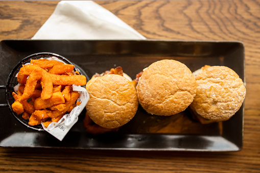 Directly above shot of three burgers with batter dipped sweet potato fries served in a black tray on a serving hatch in restaurant kitchen