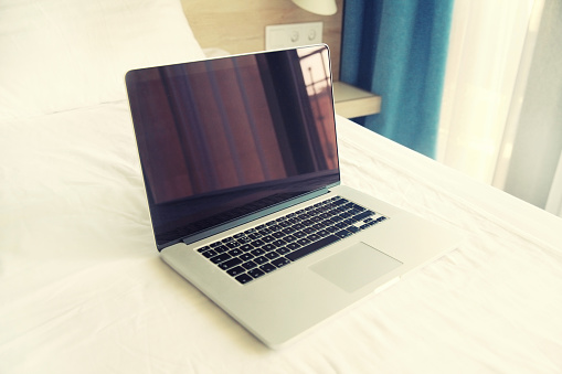 Laptop with blank black screen with smartphone and keyboard on white bed in the room