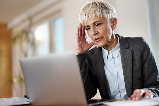 Mature female entrepreneur feeling worried while reading a problematic e-mail on a computer at home office.
