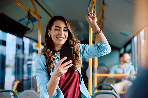 Happy woman text messaging on mobile phone while riding in a bus.