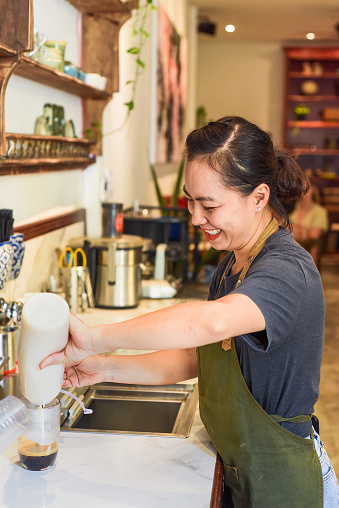 Vietnamese barista pouring condensed milk in glass cup for preparing vietnamese coffee Cafe Sua