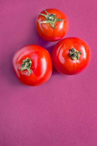 Three fresh red tomatoes on purple background