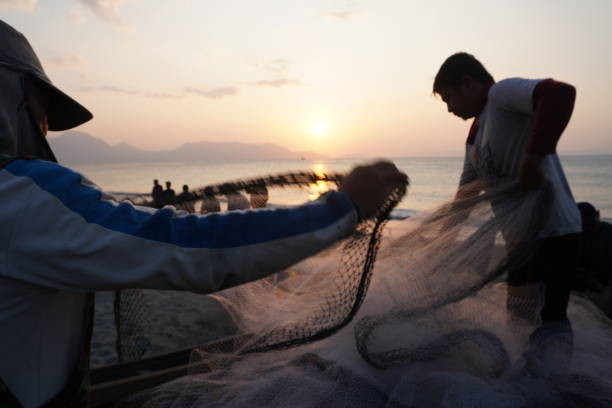 Fishermen pull their net against the sunset on a beach in Banda Aceh on March 07, 2023