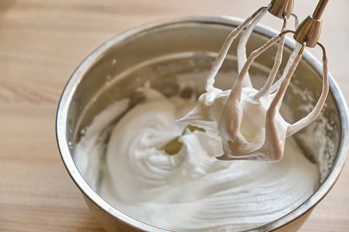 Mixer beaters with whipped egg whites. Whipped egg whites and other ingredients for cream or as an ingredient for baking on wooden table, closeup