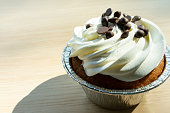 istock Vanilla muffin cake with chocolate pieces and whipped cream on foil package on wooden table in cafe. 1485334501