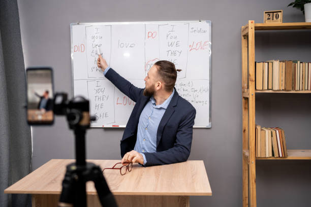 istock English teacher giving online lesson using whiteboard with grammar rules and smartphone, pointing at blackboard at home office. Tutor or coach engaged in webcam virtual class.Distant education 1485335038