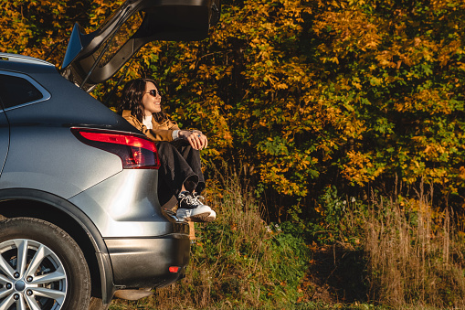 dreamy woman sits in trunk of her car and rests from long journey