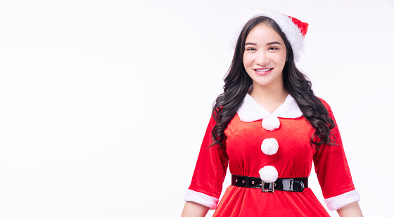 Cheerful asian Santa Claus dress with christmas hat standing holding hands on white background. Friendly Santa Claus young girl wear hat smiling look camera over isolated background. Merry christmas