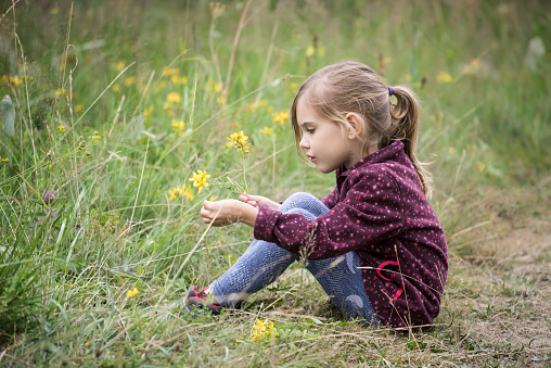 Lovely little girl playing in the green field with yellow flowers