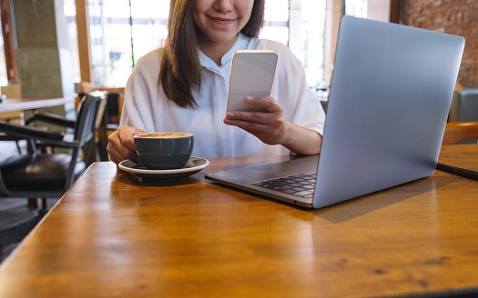 Closeup image of a young woman drinking coffee, chatting on mobile phone while using laptop computer