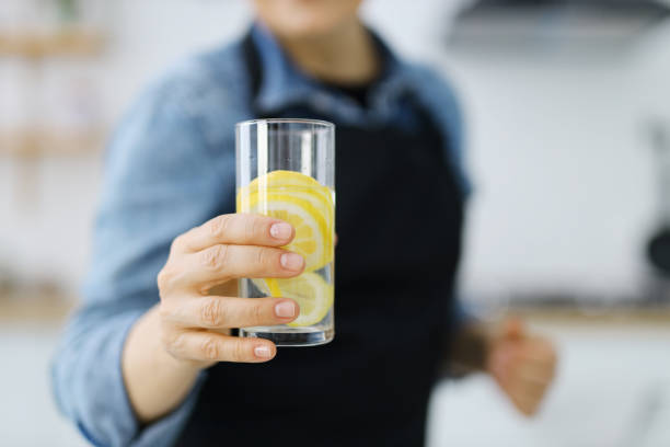 close-up, um copo de água com limão na mão de uma mulher. - close up women horizontal citrus fruit - fotografias e filmes do acervo