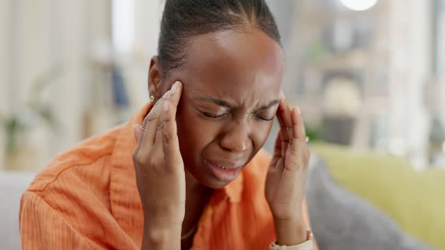Sick, massage and black woman with headache pain, stress or vertigo at home. Anxiety, sad and African girl massaging her temples for migraine relief, fatigue and mental health issue on the sofa