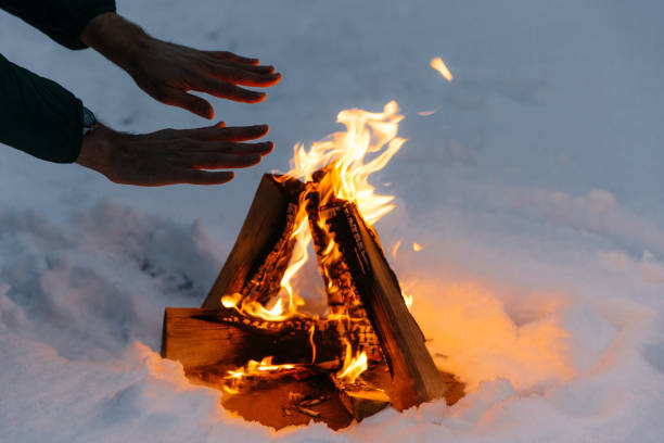 istock Unrecognizable male warms hands on fire in forest during cold winter, tries to warm himself, being cold spend time on cold snow and frosty weather. Burning flame on ground covered with snow. 1485346054