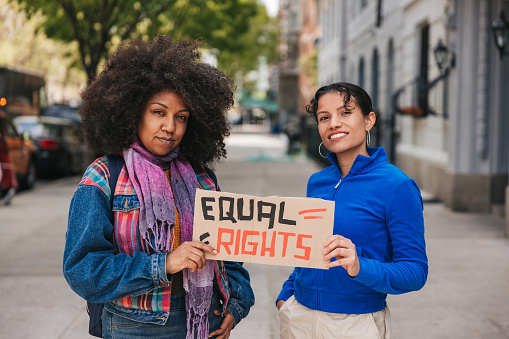 Portrait of two people holding hand-made sign on cardboard about equal rights for every person. This is a portrait taken during a march for lgbtqia+ rights. Love is love.