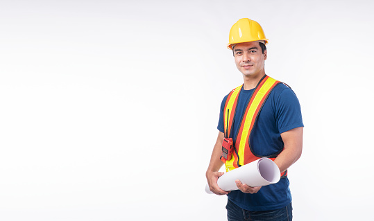 Thoughtful handsome man wear helmet safety holding blueprint standing on isolated white background. Engineer guy with walkie talkie holding plan blueprint building wear yellow hardhat white background