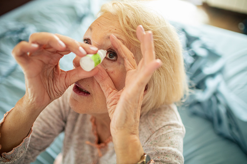 Close up of a senior woman using eye drops in the bedroom