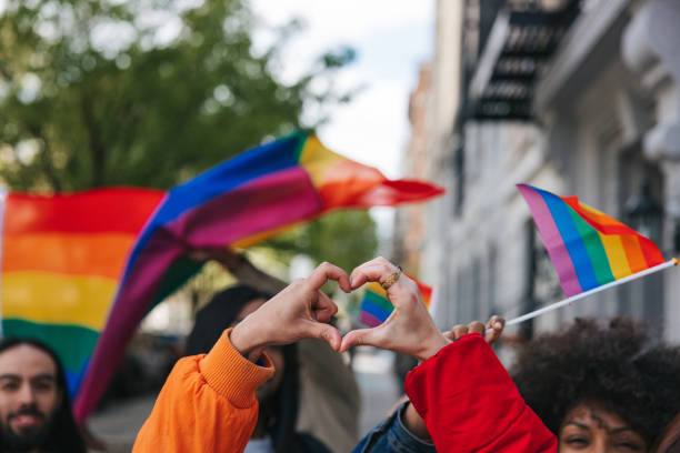 Genderqueere und nicht-binäre Freund*innen, die vor einer Regenbogenfahne eine Herzform bilden – Foto