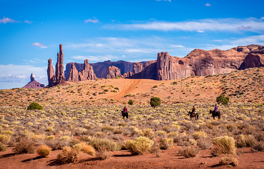 13 october 2018 - Oljato, Arizona. USA: Three unrecognizable person riding a horse tourat Monument Valley in front of Totem Pole and The Yei Bi Chei, Arizona, USA