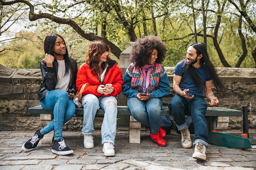 Group of friends sitting and scrolling mobile phone at the park.