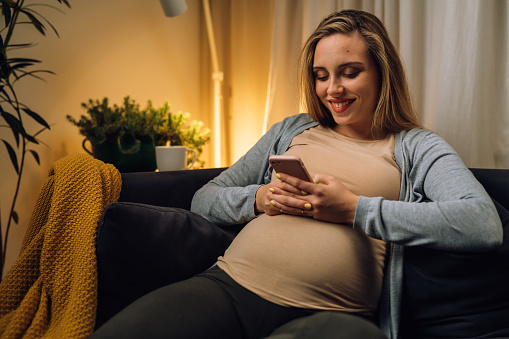 Pregnant woman sits on the sofa and looks at the phone