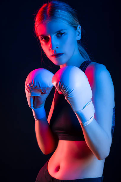 istock Winsome Active Female Boxer  Posing in White Gloves And Making Hit Against Dark Background With Colorul Lights. 1485351027