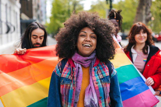 Woman with natural black hair Afro hairstyle posing in front a rainbow flags during a Pride Parade stock photo