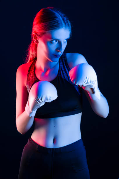 istock Winsome Active Female Boxer  Posing in White Gloves And Making Hit Against Dark Background With Colorul Lights. 1485351061