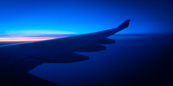 Cool blue airplane window view of the twilight landscape in the sky over the northern Atlantic Ocean, night flight photography
