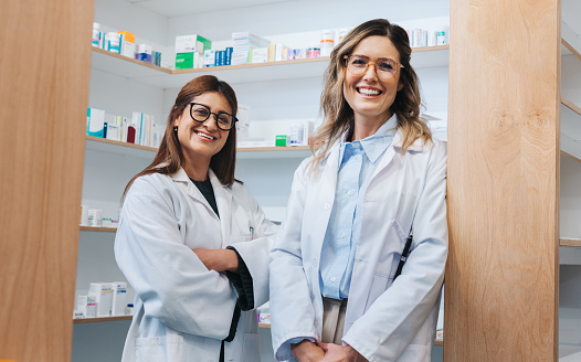 Female pharmacists standing in a chemist and smiling at the camera. Two healthcare professionals working together in a pharmacy.