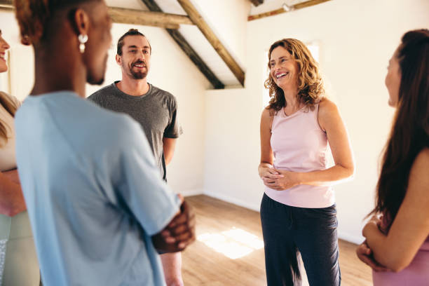 Group of people talking to a mental fitness coach in a yoga studio Group of people talking to a yoga coach while standing in a huddle. Happy people attending a mental fitness class in a yoga studio. yoga instructor stock pictures, royalty-free photos & images