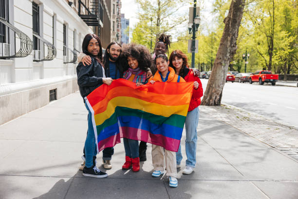 Group of friends posing with a rainbow flag before the LGBTQIA+ Pride Parade Pride parade in the city street, people of different gender and ethnicities marching celebrating freedom and love. lesbian pride stock pictures, royalty-free photos & images