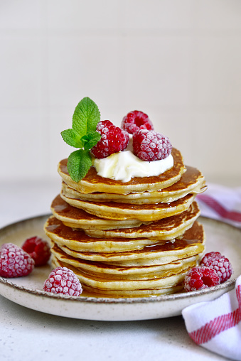 Delicious homemade pancakes with whipped cream, maple syrup and raspberry for a breakfast on a white slate, stone or concrete background.