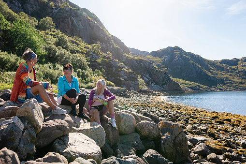 A shot of a small group of senior women sitting down at the bay on the rocks near the village of Diabaig on the side of Loch Torridon in Wester Ross, Scotland. They are taking a break from their hike to sit, relax and chat. One woman is holding a reusable water bottle.