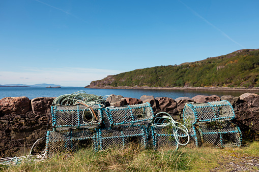 A pile of lobster traps stacked together by the bay near the village of Diabaig on the side of Loch Torridon in Wester Ross, Scotland, with a view of the sea behind.