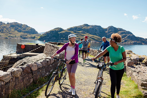 A shot of a small group of senior friends walking by the bay near the village of Diabaig on the side of Loch Torridon in Wester Ross, Scotland. They are enjoying the nice weather and laughing with each other while pushing their bikes.