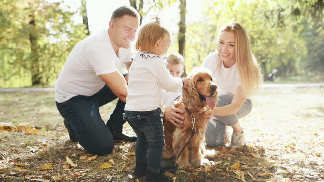 Cheerful young family have a rest in autumn park together and petting dog