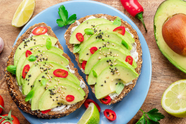 istock Avocado toasts - bread with avocado slices, pieces chilli pepper and black sesame on blue plate on wooden table. 1485363624