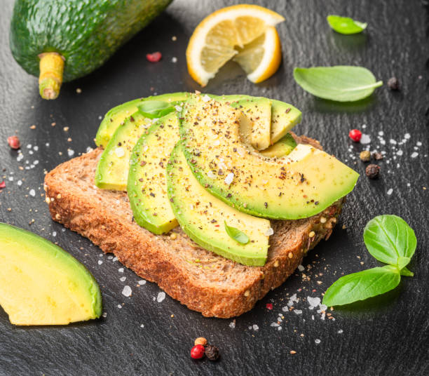 istock Avocado toast - bread with avocado slices on natural slate serving board. Top view. 1485363642