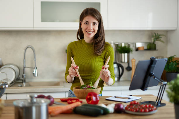 istock Young woman standing in the kitchen making a salad using online recipe 1485364595