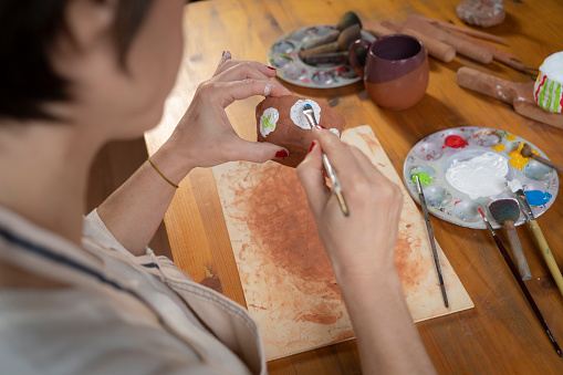 mature woman painting a pottery in workshop. Craftsperson painting a bowl made of clay in art studio