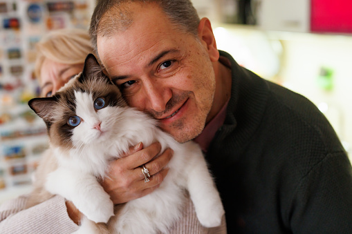 Portrait of happy mature couple hugging their ragdoll cat at home