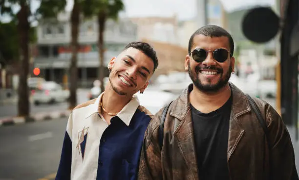 Portrait of a young gay couple smiling while standing side by side together on a sidewalk in the city