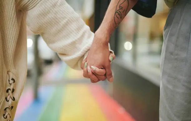 Close-up of two young friends standing in unity together on a city sidewalk painted with the pride rainbow
