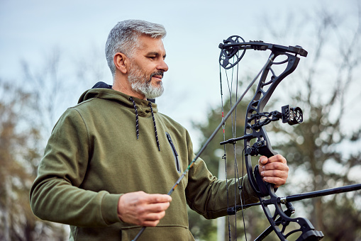 A sporty senior bearded man holding a bow and arrow, practicing shooting in archery.