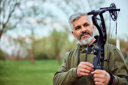 A serious senior bearded man using a bow and arrow, practicing shooting in archery.