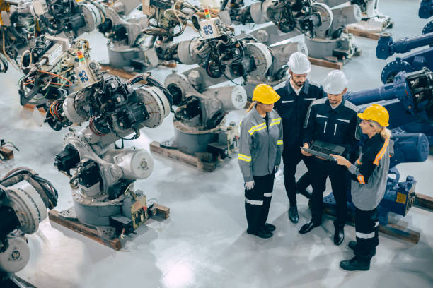 Engineer team diverse working together in modern industrial robotics factory. Engineers people teamwork standing around robot arm in machine assembly plant.