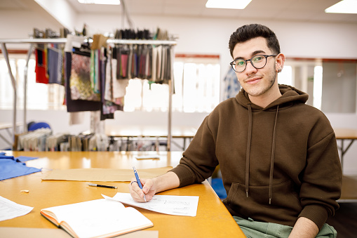 Estudiante de moda con gafas sentado junto a la mesa tomando notas photo