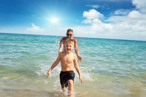 Family day. Happy dad and child having fun together outdoors, splashing sea water and laughing. Childhood and parenting concept.