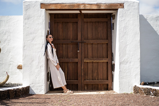 Relaxed woman standing near big wooden door, enjoying summer vacation day at the spanish island. Tourism. Traveler.