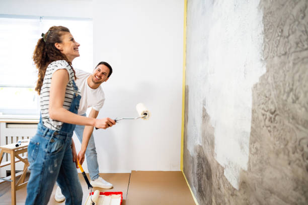 alegre pareja pintando la pared en un apartamento nuevo - home improvement couple painting real estate fotografías e imágenes de stock